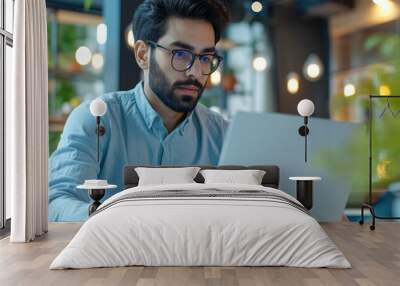 Successful young Arab businessman in glasses working on laptop at company office, typing on pc keyboard, and participating in video calls as CEO. Wall mural