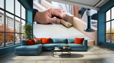 Close-up of carpenter cutting a wooden baseboard. Male carpenter sawing a baseboard with a circular saw in a carpentry workshop close-up. Using a miter saw to cut a piece of wood Wall mural