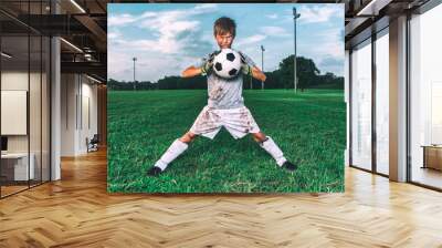 Muddy little soccer player in funny pose trying to crush soccer ball Wall mural