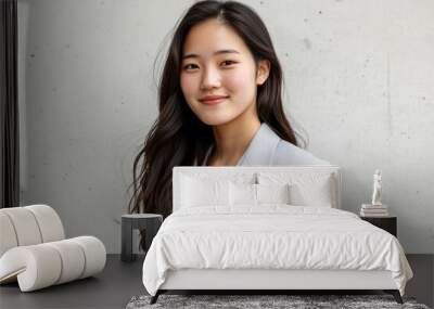 A young Japanese businesswoman wearing a light gray suit stands in front of a white wall, smiling at the camera Wall mural