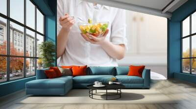 Young woman eating healthy fruit breakfast in bowl at home Wall mural