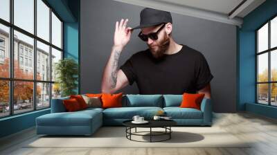 Hipster handsome male model with beard wearing black blank t-shirt with space for your logo or design over gray background Wall mural