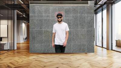 Hipster handsome male model with beard wearing white blank t-shirt and a baseball cap with space for your logo or design in casual urban style Wall mural