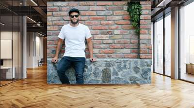 Hipster handsome male model with beard wearing white blank t-shirt and a baseball cap with space for your logo or design in casual urban style Wall mural