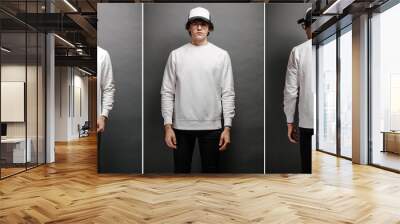 Man wearing blank white sweatshirt and empty baseball cap standing over gray background. Sweatshirt or hoodie for mock up, logo designs or design print with with free space. Wall mural