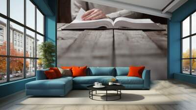 woman hands on bible. she is reading and praying over bible in a dark space over wooden table Wall mural