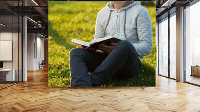 Young man reading Bible in a park.. Wall mural