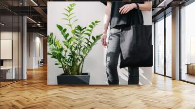 Young woman holding black textile eco bag againstwhite wall. Ecology or environment protection concept. White eco bag for mock up. Wall mural