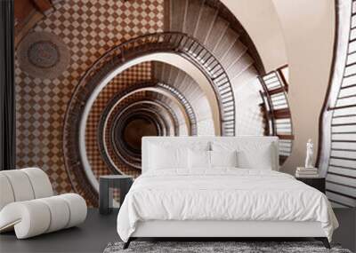 Brown round spiral staircase with white walls black railings with patterns and checkered floor down view Wall mural