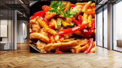 Asian cuisine, stir fry with chicken, red paprika pepper and zucchini in frying pan. Black kitchen table background, top view, close up Wall mural