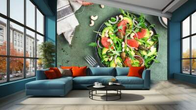 Healthy vegan salad with arugula, avocado, juicy grapefruit, cashews and dressing with olive oil, honey and wine vinegar. Green rustic kitchen table, top view, copy space Wall mural