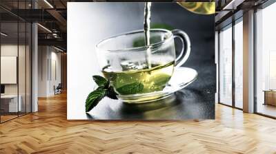 Hot chinese green tea with mint, with splash pouring from the kettle into the cup, steam rises, dark background, selective focus Wall mural