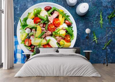 Nicoise salad with canned  tuna, tomatoes, boiled eggs, green beans, potatoes and olives on white plate, blue table background, top view Wall mural