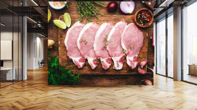 Raw pork chops, meat on rustic wooden cutting board prepared for cooking with garlic, thyme, spices and pepper. Old wood kitchen table,  top view Wall mural