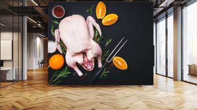 Raw whole duck with orange, pepper and rosemary. Ready to bake for a festive dinner. Black table background. Top view. Copy space Wall mural