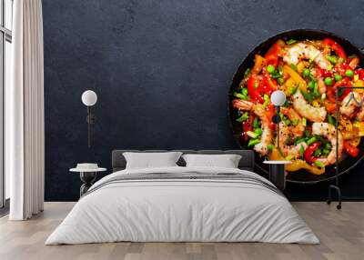 Stir fry with shrimps, red and yellow paprika, green pea, chives and sesame seeds in frying pan. Asian cuisine dish. Black stone kitchen table background, top view banner Wall mural