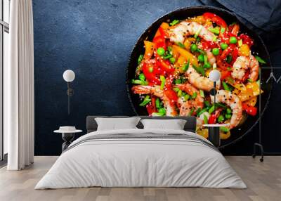 Stir fry with shrimps, red and yellow paprika, green pea, chives and sesame seeds in frying pan. Asian cuisine dish. Black stone kitchen table background, top view Wall mural