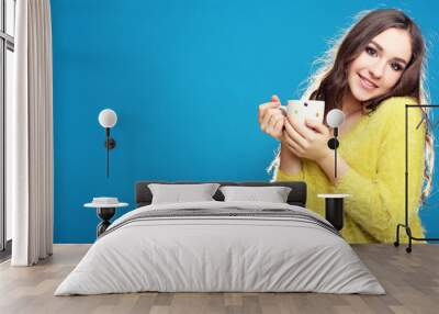 Beautiful young girl with cup of tea on blue background Wall mural