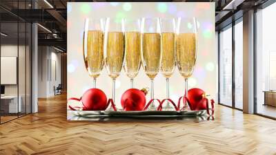 Glasses of champagne with red baubles and ribbon on blurred lights background Wall mural