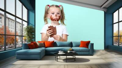 Happy little girl eating chocolate on mint background Wall mural