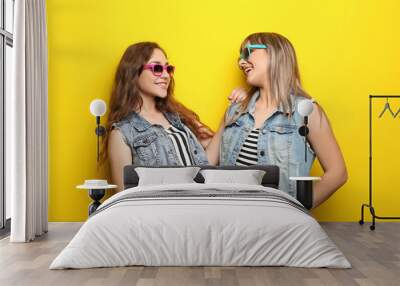 Portrait of two young woman with sunglasses on yellow background Wall mural