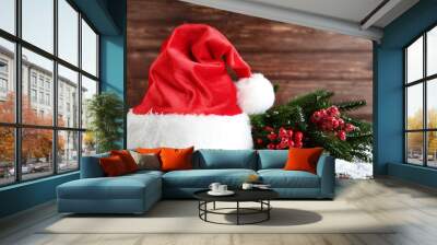 Santa claus hat and fir tree branches with red berries on wooden table Wall mural