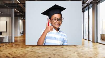 Young African American boy in graduation cap showing thumb up on grey background Wall mural