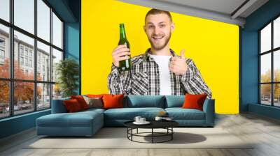 Young man with bottle of beer on yellow background Wall mural