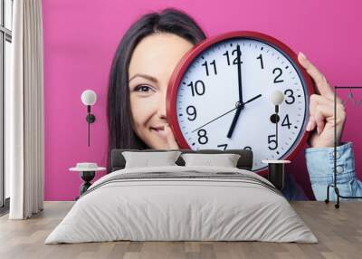 Young woman holding a clock on pink background Wall mural