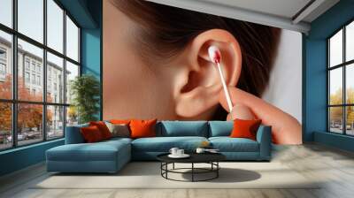 Close-up of a woman's ear as she holds a cotton swab with blood on it, against a clean background, highlighting ear care issues. Wall mural