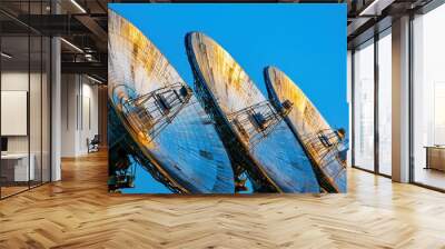 Multiple satellite dishes on an installation tower with cables, framed against the backdrop of a bright blue sky, illustrating advanced telecommunications. Wall mural