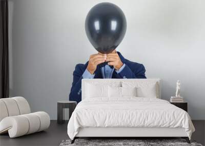 Young man hiding face behind black balloon in suit , front view. Wall mural