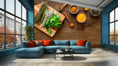 Colorful spices in wooden bowls and green herbs for cooking, top view Wall mural