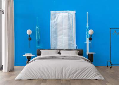 Influenza preventive tools. Medical face mask and vaccine on blue background top view Wall mural