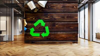 Recycling sign with waste materials, bottle, cups, can for ecology concept on wooden background top view mock up Wall mural