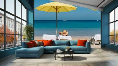 A women sitting on beach chair under colorful yellow beach umbrella with a background of beautiful Andaman sea in Phuket, Thailand Wall mural