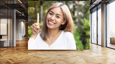 Playful happy smiling southeast asian woman with modern hair coloring pointing up one finger, one point Wall mural