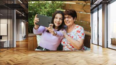 Grandmother and granddaughter taking a selfie with a tablet and laughing outdoors Wall mural