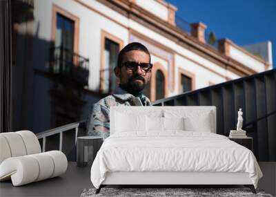 Portrait of young handsome gay man with beard and glasses. The man is dressed casually and in modern clothes and is serious and angry. Wall mural