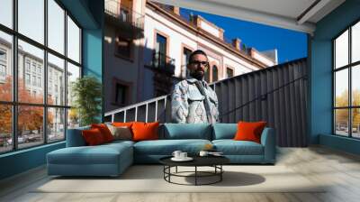 Portrait of young handsome gay man with beard and glasses. The man is dressed casually and in modern clothes and is serious and angry. Wall mural