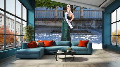 Pretty young woman winner of a beauty pageant dressed in a green sequined dress. Young woman wears diamond crown and winner's sash and poses for photo. Fashion and beauty concept. Wall mural