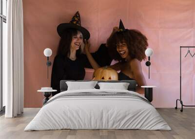 two beautiful young women, one blonde and the other African-American, dressed as witches and holding a pumpkin, are having fun at a Halloween party. The women are happy. Wall mural