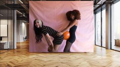 Two women, one blonde and the other Afro-American, young and beautiful, playing with orange balloon at a halloween party. Concept happiness Wall mural