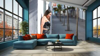 Young and beautiful woman with long brown hair dressed in black leather leaning against the white wall of Conil. The woman is on holiday in spain in cadiz. The woman is happy. Wall mural