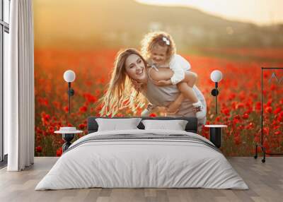 beautiful child girl with young mother are having fun in field of poppy flowers over sunset lights Wall mural