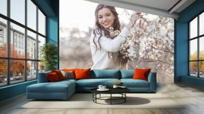 Pretty smiling teen girl are posing in garden near blossom cherry tree with white flowers. Spring time Wall mural