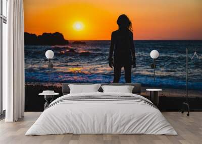 Silhouette of child in sunset on a beach. Little girl standing on sunset beach with sea in background. Wall mural