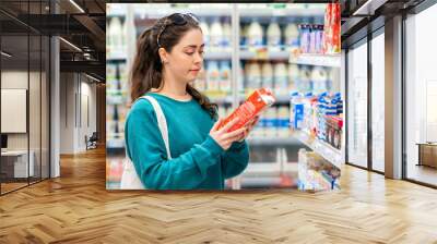 A young beautiful Caucasian woman with an eco-bag on her shoulder, reads the ingredients on the package. Concept of food purchase and shopping Wall mural