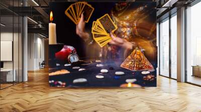 Astrology and esotericism. Magic glass pyramid with a magical glow. In the background, a fortune teller holds a fan of Tarot cards. Dark table with runes and candles. Close-up Wall mural