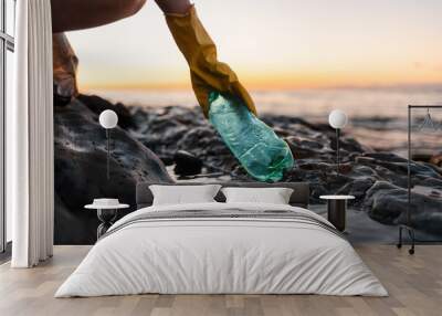 Earth day. Volunteer in protective gloves picks up a plastic bottle on the beach. Close up of hand. Low angle view. Copy space. The concept of cleaning the coastal zone Wall mural